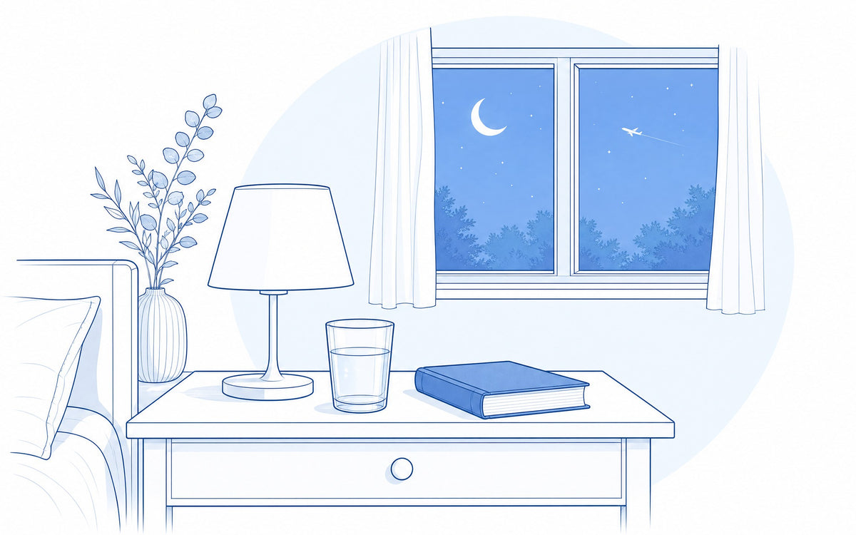 Melatonin wann einnehmen: Nachttisch mit Lampe und Wasserglas, im Fenster Mond, Sterne und ein Flugzeug
